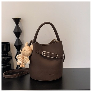 Detail of brown leather bucket bag with silver buckle and cute teddy bear charm