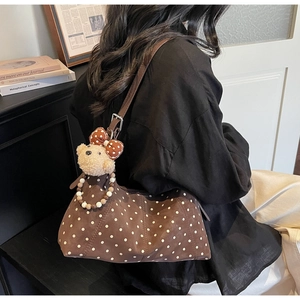 Detail of dark brown polka dot shoulder bag featuring a plush teddy bear charm accessory