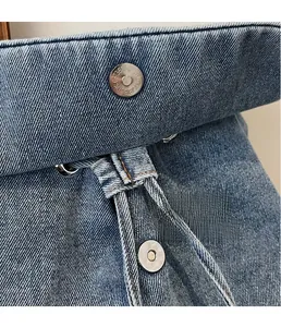 Macro detail of silver magnetic closure on blue denim backpack with contrast stitching