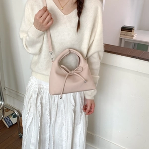 Detail of light pink crossbody bag with bow drawstring and adjustable strap on model