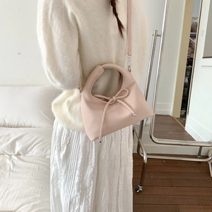 Pink crossbody bag with leather bow decoration shown on model in home setting