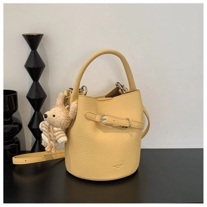 Detailed shot of yellow bucket bag featuring pebble leather texture and a bear charm