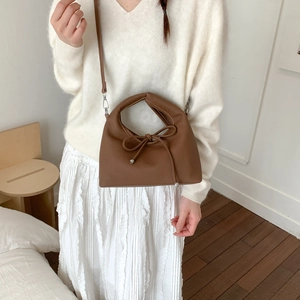Brown leather dumpling bag with bow detail held by a model in a minimalist setting