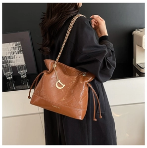Détail du sac seau marron avec bandoulière chaîne dorée et texture élégante en cuir matelassé
