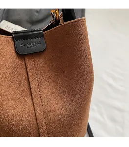 Close-up of brown suede bucket bag featuring high-quality stitching and leather brand tag