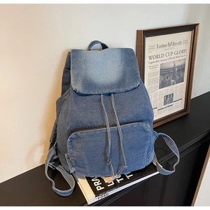 Detail of blue denim backpack showing drawstring closure and front zipper pocket texture