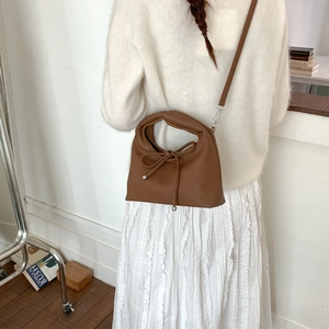 Detail view of brown leather crossbody bag with bow drawstring on model in cozy outfit