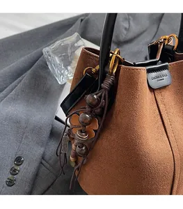 Close-up of brown suede bucket bag with black leather handle and vintage floral pendant charm