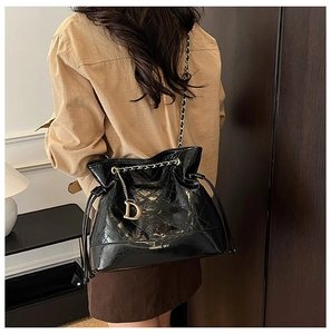 Détail d'un sac seau matelassé noir brillant avec pendentif D doré et chaîne