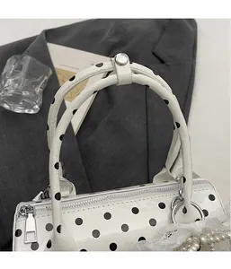 Detailed close-up of white polka dot cylinder handbag with pearl lace charm and silver zipper