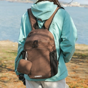 Outdoor shot of a brown plaid nylon backpack with a matching small hanging coin pouch