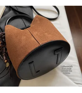 Detail of brown suede bucket bag featuring anti-wear bottom pads and black ring handles