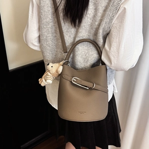 Detail view of the pebbled leather bucket bag with a knitted bear charm and silver hardware