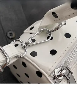 Detailed close-up of silver metal hooks and zipper on a white polka dot barrel bag