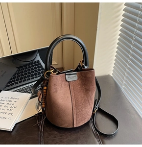 Detail of a dark brown suede bucket bag featuring black leather trim and decorative charm