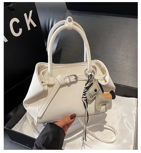 Detalle del bolso de mano en cuero blanco tipo trapecio con doble asa y adorno móvil