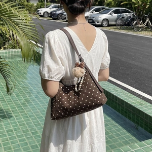 Brown polka dot shoulder bag with cute lamb plush charm worn by model in white dress