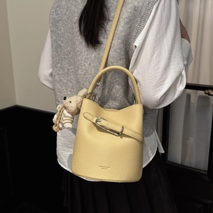 Detail of light yellow bucket bag in pebble leather with a cute brown knit bear charm