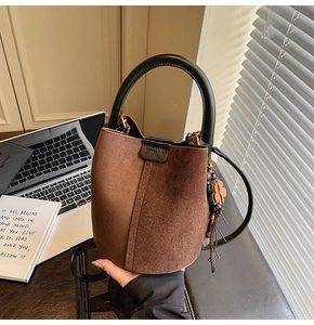 Brown suede bucket bag with wooden bead tassel and clover charm in a desk setting