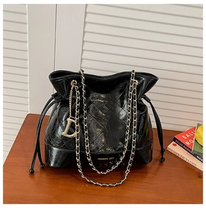 Détail d'un sac seau plissé noir avec chaîne dorée et pendentif D sur table en bois