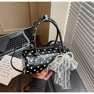 Detailed close-up of a black polka dot cylinder bag with pearl bow and lace accents