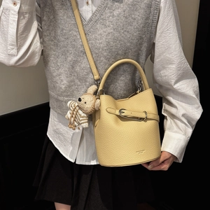 Detail view of yellow lychee grain bucket bag with brown teddy bear charm and strap