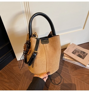 Detail of a brown suede bucket bag with round handles, metal locks, and a floral charm