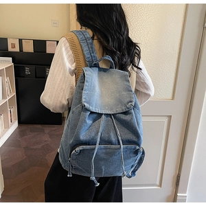 Detail view of washed denim backpack featuring a front zipper pocket and drawstring closure