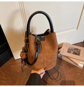 Close-up of brown suede bucket bag with black leather handle and clover charm detail
