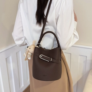 Detail of dark brown leather bucket bag with handle, shoulder strap and bear charm