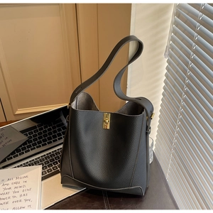 Détail du sac seau en cuir gris foncé avec fermoir rotatif doré sur un bureau de travail