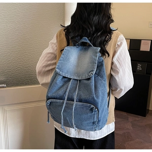 Detailed view of vintage blue denim backpack with drawstring flap and front zipper pocket