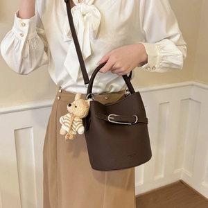 Detail of dark brown lychee leather bucket bag featuring a cute teddy bear charm