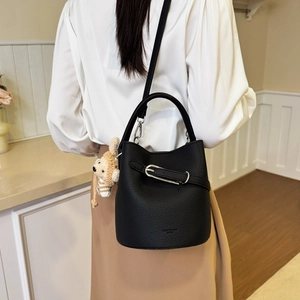 Detail of black bucket bag showing litchi grain leather and cute doll pendant accessory