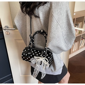 Close-up of black polka dot cylinder bag with lace bow and pearl charm detail