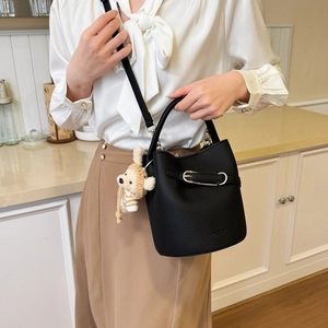 Detail of black lychee grain bucket bag with silver buckle and plush bear charm