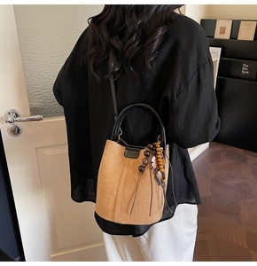 Detail of tan suede bucket bag featuring black leather handle and ethnic wood bead charm