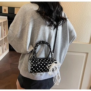 Polka dot barrel bag with pearl bow charm held by a person in a vintage bookstore setting