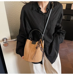 Detail view of brown suede bucket bag with black leather straps and retro tassel charm