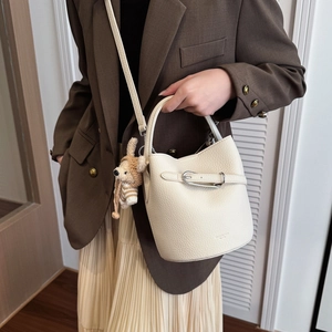 Close-up of beige lychee leather bucket bag with a cute brown knitted bear charm