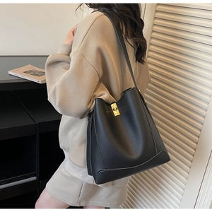 Détail d'un sac seau en cuir noir grainé avec fermoir doré porté par un mannequin