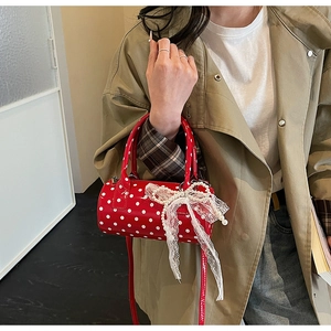 Close-up of a red polka dot cylinder bag with lace bows and pearl charms held by a model