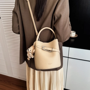 Close-up of beige leather bucket bag with lychee texture and cute bear charm