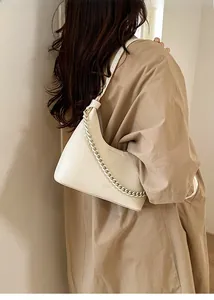 Chic beige crescent bag with textured leather and chain detail worn with a trench coat