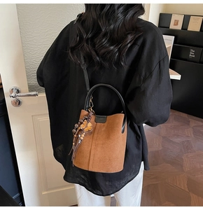 Detail of a brown suede bucket bag with bohemian tassel and black leather handle