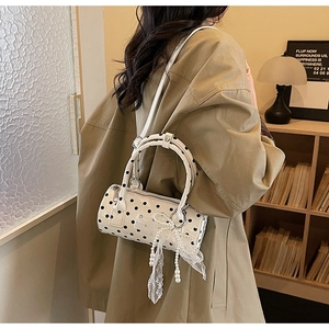 Detailed close-up of white polka dot cylinder bag with lace and pearl bow decoration