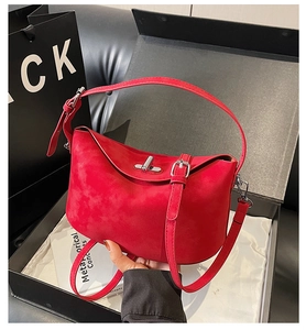 Detailed close-up of a bright red suede handbag with metal twist lock and luxury gift box
