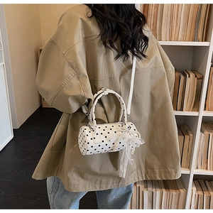 Close-up of white polka dot cylinder bag with lace bow and pearl bead pendants