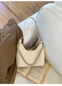 Detail of creamy white litchi pattern leather bag with decorative chain on a sofa