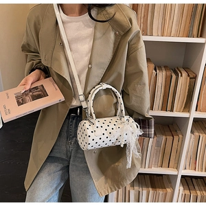 Detailed close-up of a white polka dot cylinder crossbody bag with pearl lace bow detail